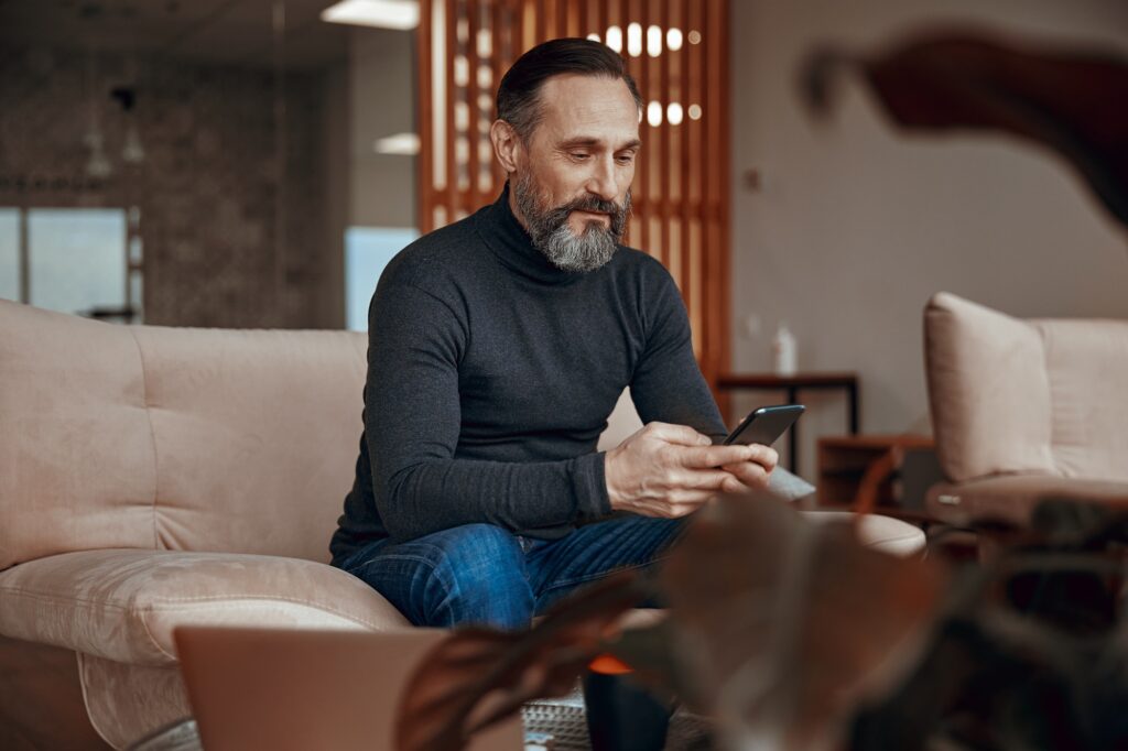 Adult man sitting in armchair and using phone