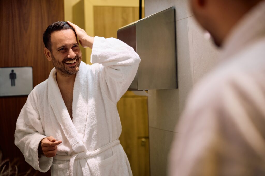 Reflection in a mirror of happy man doing his hair in the bathroom.